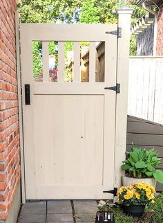 a white wooden gate with flowers in pots on the ground next to it and a brick wall behind it