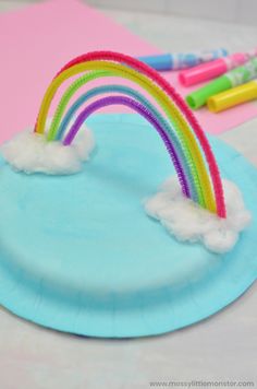 a paper plate with rainbows and clouds on it next to crayon markers