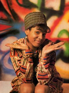 a young man sitting on top of a wooden bench in front of a graffiti covered wall