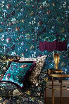 a couch with pillows and a lamp in front of a floral wallpapered wall