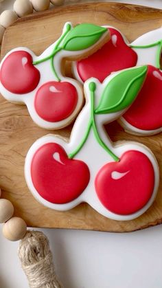 decorated cherry cookies sitting on top of a wooden cutting board