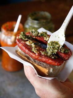 a hand holding a sandwich with pesto on it and a plastic fork sticking out of it