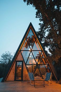 a - frame cabin in the woods at night, with chairs and lights on it