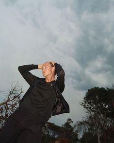 a man standing in front of a cloudy sky with his hand on his head looking up