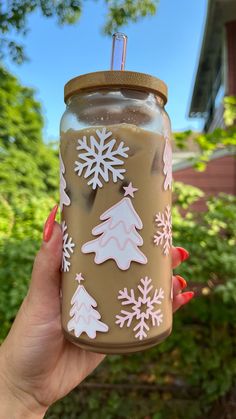 a person holding up a mason jar with snowflakes on it in front of some trees