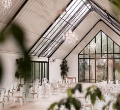 an indoor dining area with white chairs and chandelier hanging from the ceiling, surrounded by greenery