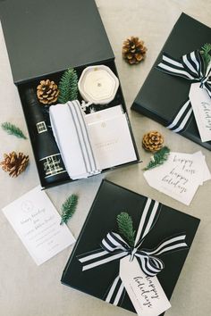 three black and white boxes with christmas cards in them next to pinecone cones