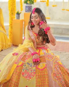 a woman in a yellow and pink dress sitting on the ground with flowers around her head