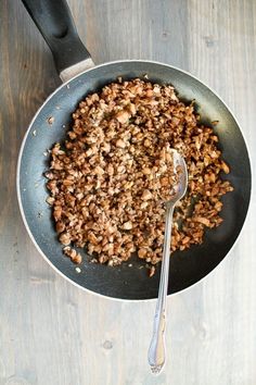 a frying pan filled with cooked food on top of a wooden table next to a spatula