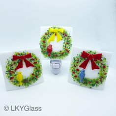 three glass magnets decorated with christmas wreaths and birds on them, one has a cell phone in the middle