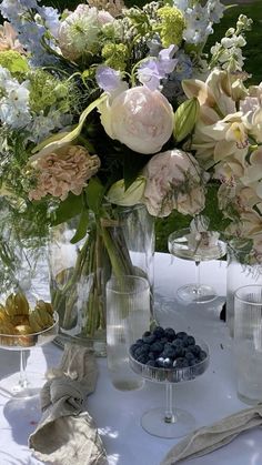 a table topped with vases filled with flowers and blueberries next to wine glasses