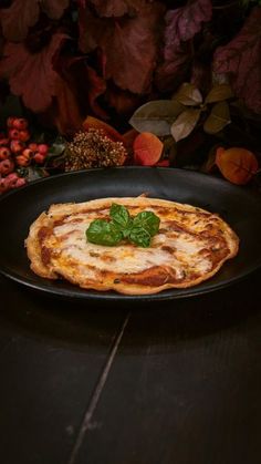 a pizza sitting on top of a black plate covered in cheese and spinach leaves