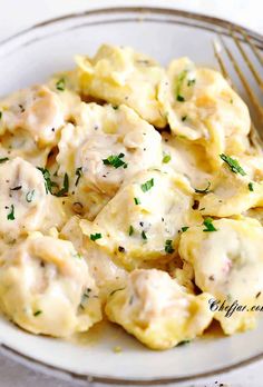 a white plate topped with ravioli covered in gravy and garnished with parsley