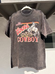 Embrace classic cowboy style with this dusk black vintage washed Coors Cowboy T-shirt. This black T-shirt features a retro Coors design, bringing together rugged Western charm and everyday wearability. Gender: Unisex Model: Regular Fabric: 100% Cotton Fabric Weight: 6.5 oz/yd² (220 g/m²) Fabric Thickness: Moderate Fabric Stretch: Slight stretch Care Instructions: Handwash or machine wash at a maximum temperature of 40℃ (105F) Do not bleach Iron on low heat Regular dry cleaning Tumble dry Feature Black Washed Graphic Tee T-shirt, Black Washed Graphic Tee, Black Western Crew Neck Top, Black Western Top With Graphic Print, Retro Black Soft-washed T-shirt, Black Short Sleeve Western Tops, Black Western Style T-shirt For Rodeo, Vintage Washed Black Stonewashed T-shirt, Retro Stonewashed Short Sleeve T-shirt