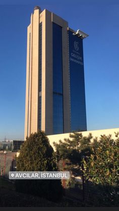 an office building in the middle of a city with trees and bushes around it on a sunny day