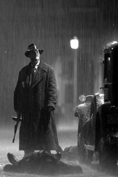 a man standing in the rain next to an old car