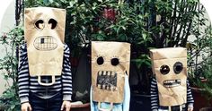 two people wearing paper bags with faces on them, standing in front of some plants