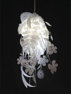 a white light hanging from a ceiling with paper flowers and leaves on it's side