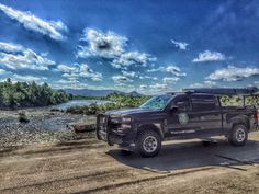 a black truck parked on the side of a dirt road next to a body of water