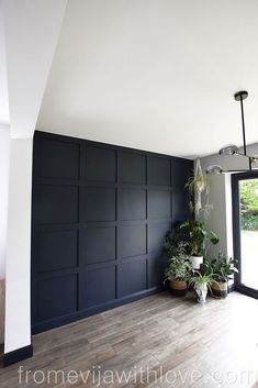 an empty room with wooden flooring and black painted paneling on the walls, along with potted plants