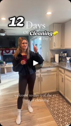 a woman standing in a kitchen holding a cup and giving the peace sign with her hand