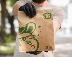 a man in black gloves holding a brown paper bag with green designs on the side