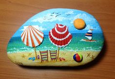 a painted rock with chairs and umbrellas on the beach next to an orange ball