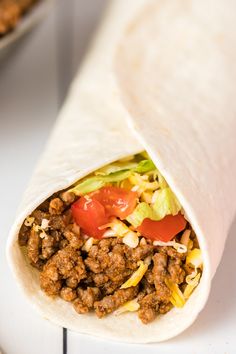 a burrito filled with meat, lettuce and tomato on a white surface