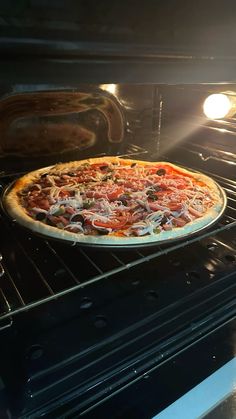 an uncooked pizza sitting in the oven with light coming through it's door