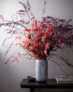 a vase filled with red and purple flowers on top of a wooden table next to books