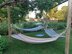 two hammocks are sitting in the grass under a pergolated arbor with blue and white stripes