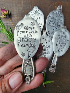 a person holding three silver spoons with writing on them and flowers in the background