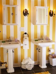 a bathroom with yellow and white striped wallpaper, two pedestal sink basins and mirrors