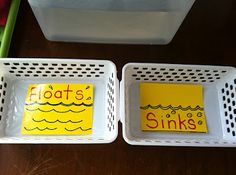 two white baskets with yellow labels on them sitting on a wooden table next to a plastic container