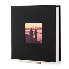 two people holding hands walking on the beach at sunset with an open book in front of them