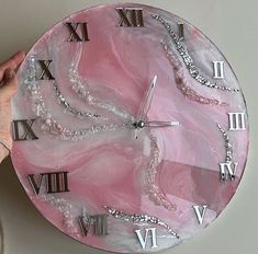 a pink clock with roman numerals and chains on the face is being held by a person's hand