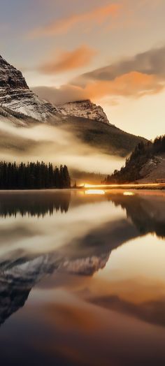 the sun is setting over a lake with mountains in the background and fog covering the water