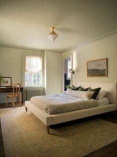 a bedroom with a large bed and two windows in the corner, along with a rug on the floor