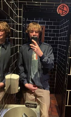 two men standing in front of a bathroom mirror taking a selfie with their cell phone