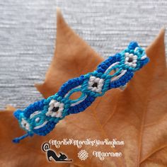 a blue and white crocheted bracelet sitting on top of an orange maple leaf