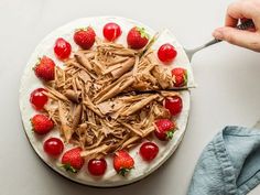 someone is cutting into a cake with chocolate frosting and strawberries on the side