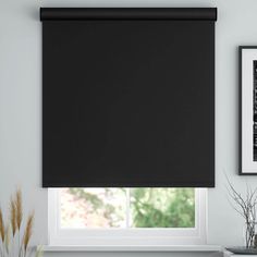 a black roller shade in a white room with pictures on the wall and window sill