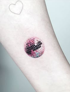 a small pink disco ball tattoo on the left inner arm, with a white heart in the background