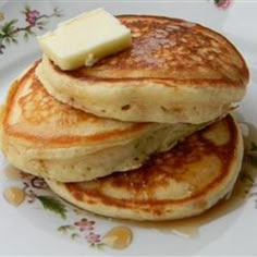 stack of pancakes with butter and syrup on a floral plate, ready to be eaten