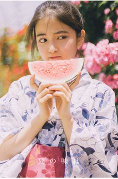 a woman holding a piece of watermelon in front of her face and looking at the camera