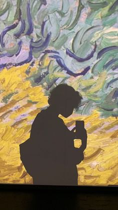 a man standing in front of a painting holding a coffee cup and looking at his cell phone