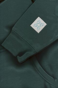 the back of a dark green sweatshirt with a white and blue patch on it's chest