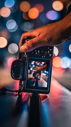 a person holding a camera with blurry lights in the background