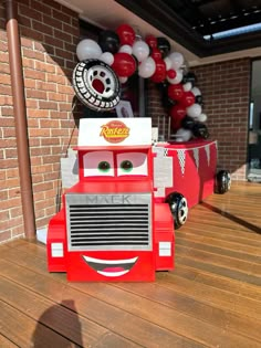 a cardboard fire truck is sitting on the ground in front of a brick wall and balloons