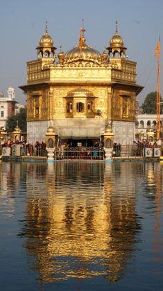 the golden building is reflected in the water near other buildings and people standing around it